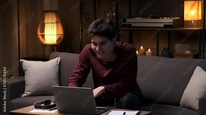 Young positive businessman working, smiling student studying remotely with laptop at home in the evening. Online work at home, remote study, friendly businessman or student.