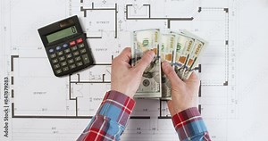 Designer counts cash money and marks total on calculator over floor plan view from above. Builder with dollar bills on printout drawing