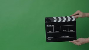 black and white film clapperboard or movie slate being held in front of a green screen. Essential filmmaking tool is used to mark scenes and synchronize audio and vid in film production.
