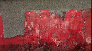 Textured red wall with peeling paint, revealing layers of history and age in urban environment
