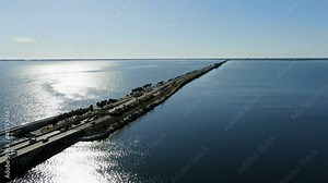 Drone Aerial Zoom Out Over Blue Bay Water and Palm Trees Towards a Bridge with Traffic and Skyline in the Distance. Late Afternoon and Palm Trees are Silhouetted. Clearwater Memorial Causeway FL