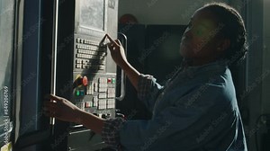 African American female industrial machine operator using control panel to set up equipment for manufacturing at plant