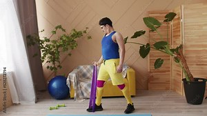 Fitness man with a moustache, glasses and headband in blue, yellow and purple retro sportswear doing workout exercise with resistance band biceps curl at home. Positive motivation sport indoors
