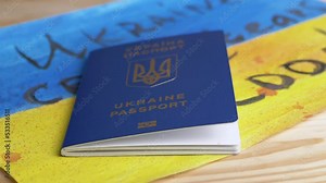 Hand Thrown a Biometric Passport of Ukraine on Table with of Ukrainian Flag. Child drawing of yellow, blue Ukrainian flag with inscription Ukraine cries tears of blood lies on table. War, migrants.