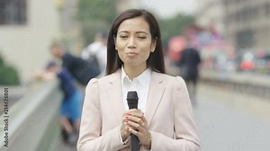 Young asian female news reporter reporting to camera in the city