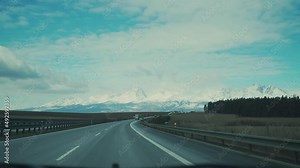 POV from driver seats car moving by highway near snow capped high mountains. Concept of journey and travelling around world