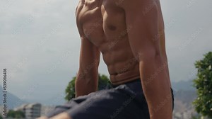 Man flexing abs on parallel bars in gym. Working on his core. Full length shot of a handsome and muscular young man working out on a dip bar outdoor