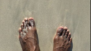 Close up view of an adult black male looking at his feet while standing on the beach. African American black male feet. Close up view of veins and arteries on a human feet.
