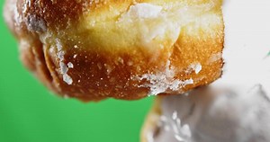 Donut with dripping white icing. Stock clip. Close-up baking with stream of white cream. White cream drips from bun on green background. Baking and cooking