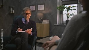 Mature psychologist takes notes, listens to patient, provides behavior therapy in modern and stylish psychological office. Counseling session with psychotherapist. Psychology and mental health concept