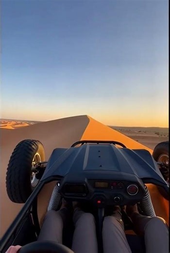 An off-road buggy climbing a tall sand dune during golden hour.
