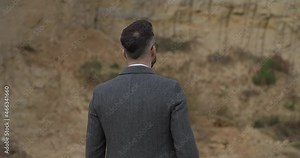 attractive bearded man with grey coat looking around, rotating and moving in a back view position and admiring nature