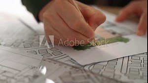 A video of architect with triangle ruler and pencil to measure blueprint. Architect designing house construction on a table at studio, architectural plan scattered around. Focus on hand. Delineation.