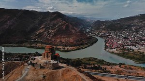Mtskheta, Georgia: Captivating aerial scenery showcasing the stunning Jvari Monastery nestled amidst majestic mountains and overlooking a meandering river. Drone view of an idyllic tourist destination