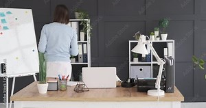 Businesswoman keeping file on shelf and using laptop at office desk