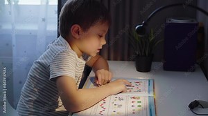 Little boy doing homework at home. kid reading a book at the table by the light of lamp. High quality FullHD footage