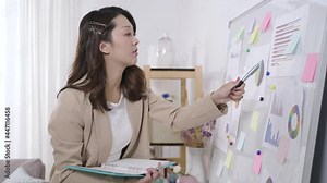 focused female employee pointing at the document on whiteboard with pen and transcribing data onto her notebook. background light office interior