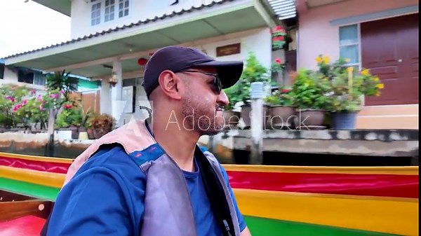 Man wearing sunglasses and a cap enjoying a long tail boat ride in Bangkok