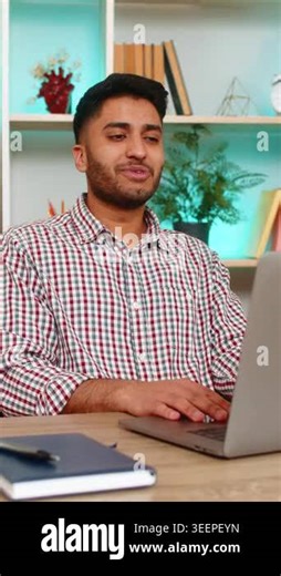 Indian man on home table smiles and waves to laptop camera during online meeting or remote lesson. Arabian boy on home table enjoys video call greeting student client or colleague with friendly mood.