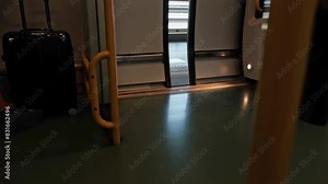 Train doors open and close, and travelers are coming in and out. There is a travel suitcase.