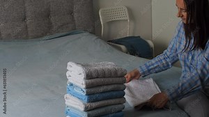Woman folding clean terry towel in the bedroom. Organizing laundry at home. Towel after washing. Concept of minimalism lifestyle and japanese folding system. Tidy up wardrobe