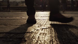 A man walks across the street during sunset with the light reflecting off the pavement | Premium Stock Video Footage