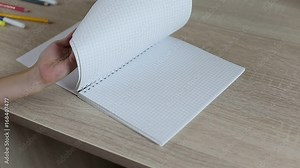 Girl's hand open notebook. Close up shot of ruled paper notebook with empty sheets. Desk table and girls hand take sheets of notebook. Concept back to school. Blured background.
