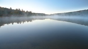 Wide angle view of Spruce Knob Lake in Appalachian mountains of Canaan valley in West Virginia with sunrise morning mist fog floating above water in Monongahela National Forest in autumn fall season