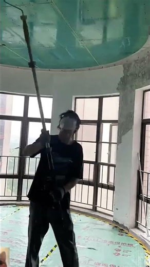 applying paint to the ceiling using a long extension pole with a roller in a room under renovation
