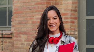 Close up individual portrait of a pretty hispanic female student smiling and looking at camera at high school. Head shot of latin teenage girl standing outdoors at the university campus. Education