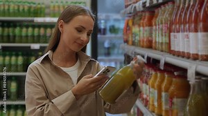 A woman buys green juice in the fruit and vegetable department of her grocery store and reaches for it. Scans the barcode of the juice label.