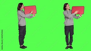 Male model poses with speech bubble, presenting blank cardboard with copyspace against full body greenscreen. Asian person holding red carton board for marketing advertisement.