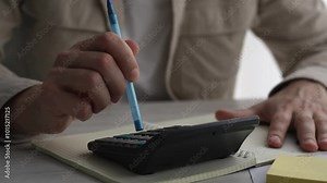 Close-up of a man calculating monthly income and results using a calculator, checking electronic bills in an e-banking computer application, managing expenses and household cash payments