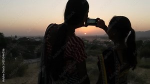 Two women silhouette against the setting sun mobile phone photo video teamwork romantic viewpoint love bonding together tourist rural setting friends handheld stabilized lovers follow escape surreal