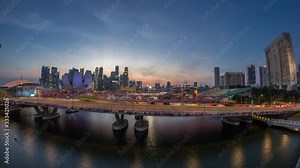 Aerial view over Helix Bridge and Bayfront Avenue with traffic day to night transition timelapse at Marina Bay from above with skyscrapers skyline on a background, Singapore. Floating stadium on the