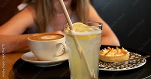 Woman with citrus lemonade, small cake and coffee cup on table. Lady guest orders refreshing drinks and snack in restaurant. Healthy lunch