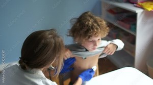Pediatrician listens to the lungs of the child using stethoscope. Boy coughs, blue gloves, international doctor's day