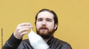 an adult man in a disposable mask sneezes. Instructions on how to wear a respirator and mask correctly, protect your loved ones with self-isolation and precautions during coronavirus.