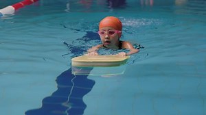 Cute Little Girl Learns To Swim. Child Training With Swimming Board Kickboard In The Pool. High Angle Tracking Shot