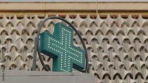 Pharmacy sign outside. Neon medical bright shining glowing green illuminated urban pharmacy drug store. Green cross indicating the location of a pharmacy. LED Pharmacy Cross Sign Animated Advertising.