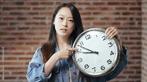 serious young Asian girl holding big clock in hands and showing the time