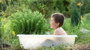 A 4-year-old boy bathes in a bath outdoors in the garden. summer fun in the backyard. What to do with a child in the summer, playing with water