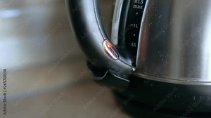 Close up man's finger turn on the stainless steel kettle. Indicator lights up