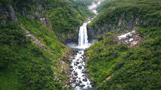 A waterfall flowing through a vast green valley