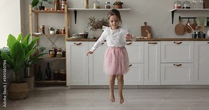 Cute barefooted little girl in pink ballet skirt dancing to music at home, jumping, hopping, training choreography, enjoying activity alone. Active energetic kid enjoying leisure, motion, smiling