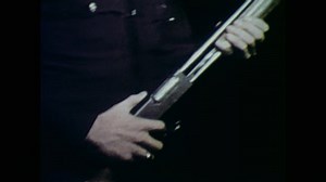 1970s: Policemen walk across yard at night, hold guns.