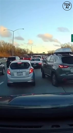 Dramatic dashcam footage recorded on a busy highway in Atlanta captures a chaotic traffic backup after a merging vehicle collides with another car, briefly appearing to ride up on top of it. The video shows congested traffic moving slowly when the sudden impact brings multiple lanes to an abrupt stop. As drivers react in shock, vehicles quickly begin backing up across the highway, with hazard lights flashing and motorists exiting their cars to assess the damage. The unusual angle of the crash le