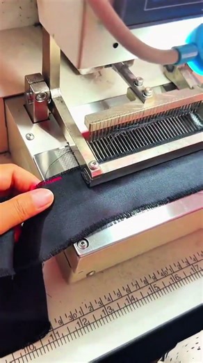 Machine presses black fabric under guided ruler scale for stitching alignment