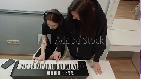 Music teacher showing young student how to play electronic keyboard, helping her by placing fingers on the correct keys, during a private music lesson