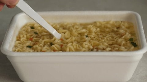 close up delicious instant noodle soup in plastic bowl eaten with plastic fork. instant noodles on kitchen table